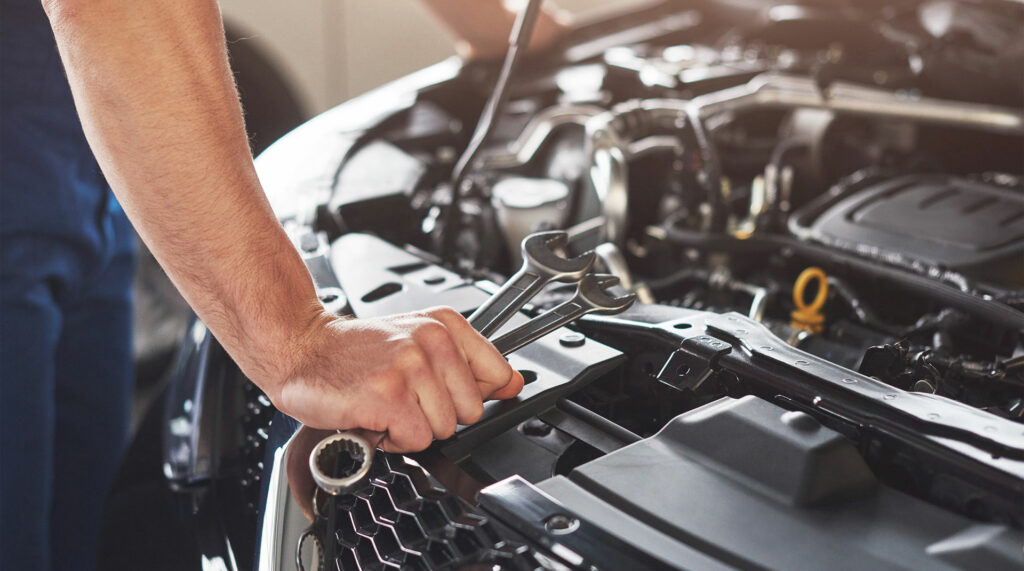 Meccanico al lavoro sul vano motore con chiavi inglesi